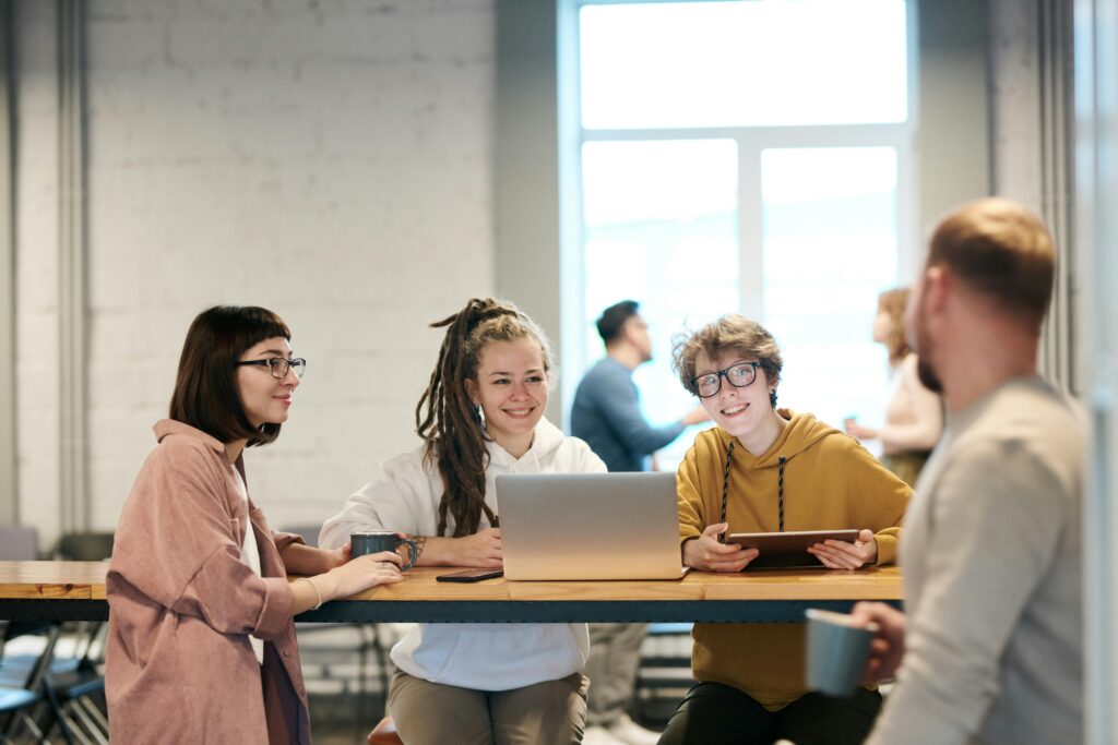 A diverse group of young professionals brainstorming in a modern office setting, discussing ideas with laptops and tablets.